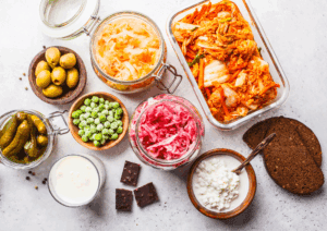 A colourful flat-lay of fermented foods including sauerkraut, kimchi, pickles, kefir, cottage cheese, olives, and rye bread, showcasing gut-friendly foods rich in probiotics to support thyroid and digestive health.