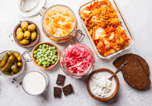 A colourful flat-lay of fermented foods including sauerkraut, kimchi, pickles, kefir, cottage cheese, olives, and rye bread, showcasing gut-friendly foods rich in probiotics to support thyroid and digestive health.