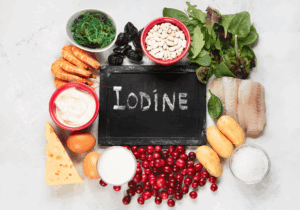 Foods rich in iodine including shrimp, fish, seaweed, dairy, eggs, cheese, cranberries, beans, potatoes, leafy greens, and iodised salt — displayed around a chalkboard with the word ‘Iodine’ written on it.